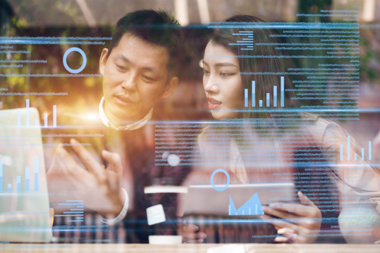 Man and woman work on screen while AI screen appear in front of them.