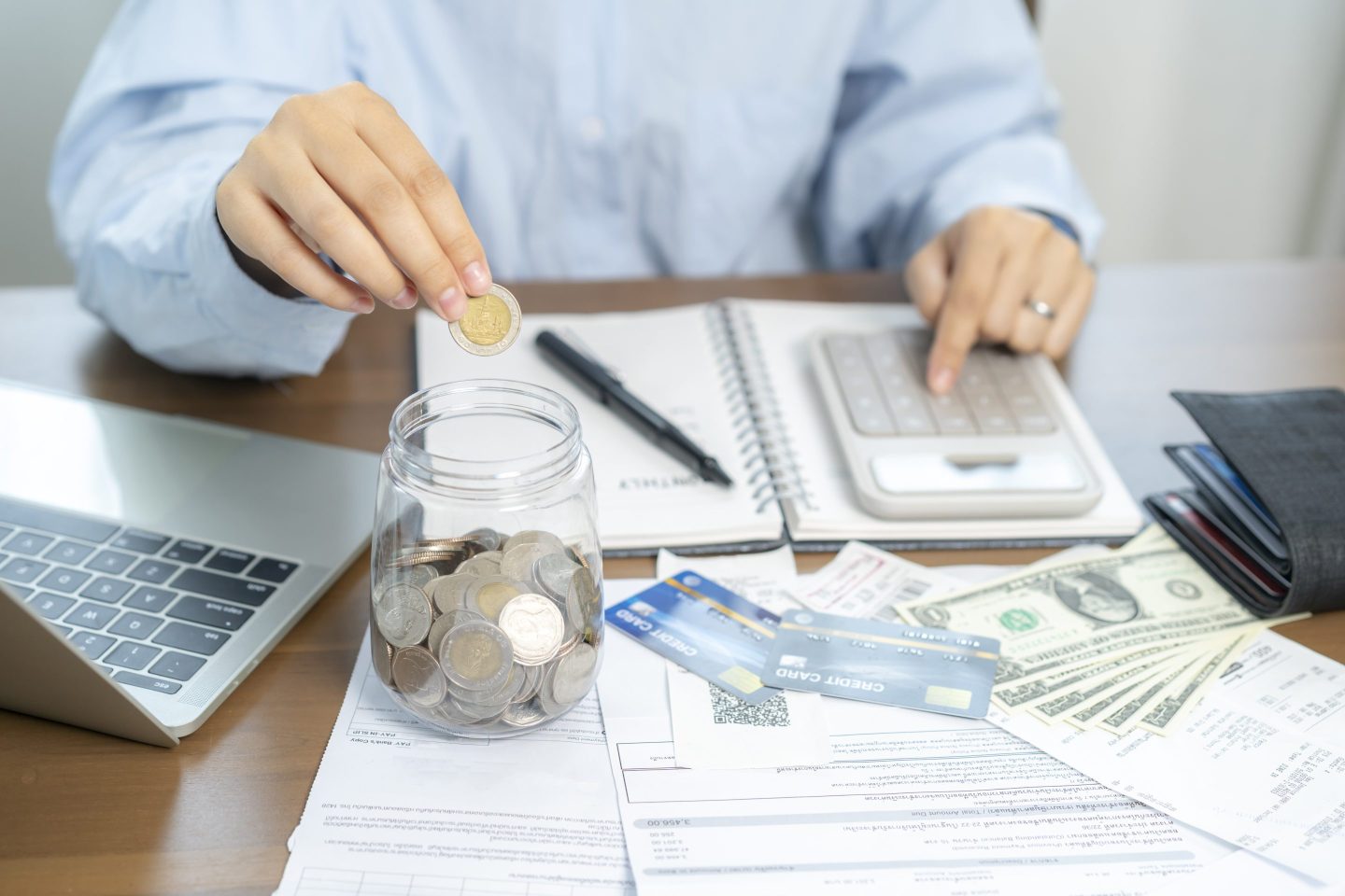 Person uses a calculator with money and coins in a jar in front of them.