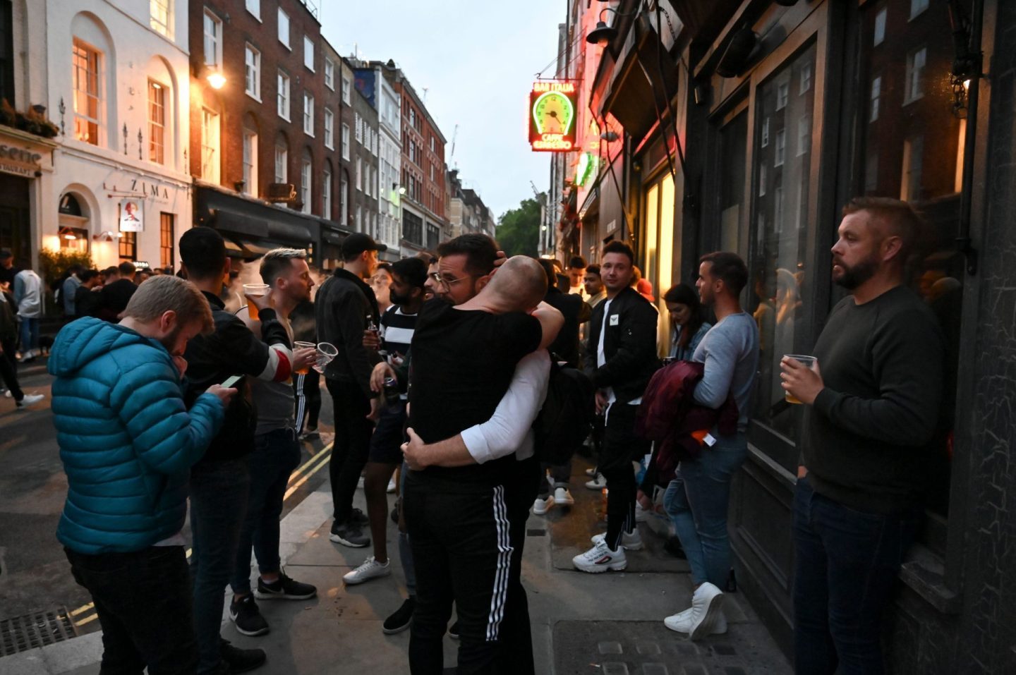 Revellers embraces as in the street outside bars in the Soho area of London on July 4, 2020, as restrictions are further eased during the novel coronavirus COVID-19 pandemic. - Pubs in England reopen on Saturday for the first time since late March, bringing cheer to drinkers and the industry but fears of public disorder and fresh coronavirus cases.