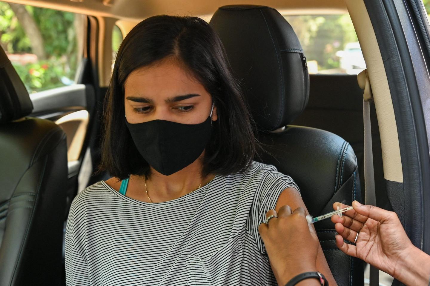 A woman sitting in a car wearing a mask and receiving a COVID-19 vaccine at a drive-through vaccination center in India.