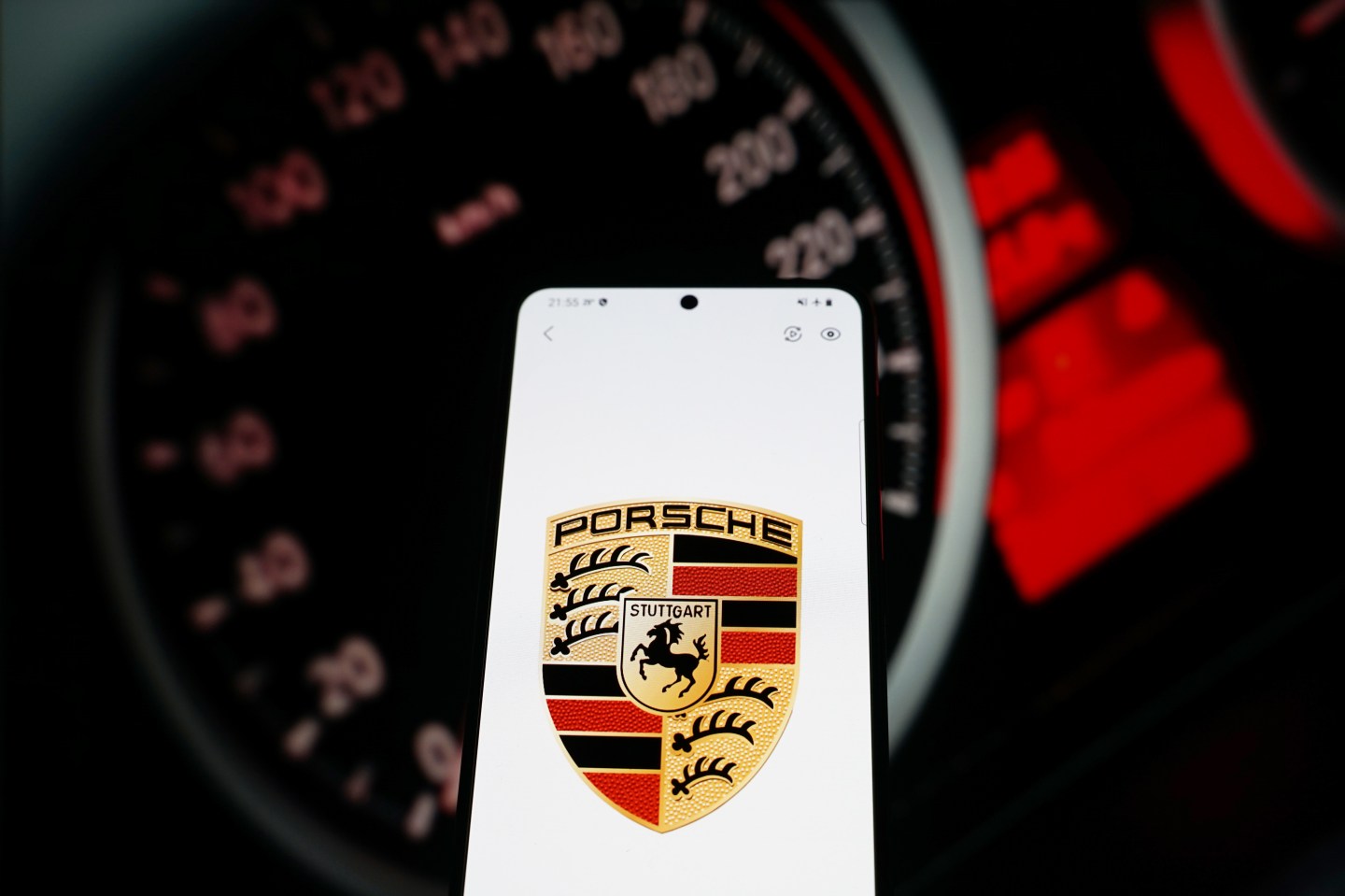 In this photo illustration a car brand logo "Porsche" seen displayed on a smartphone with car dashboard in the background.