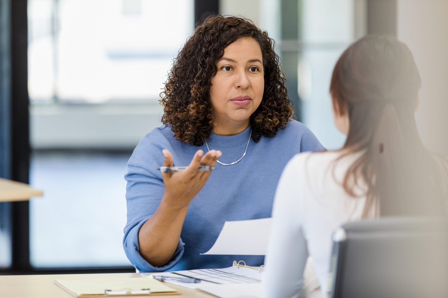 Woman talks to another woman across a desk.
