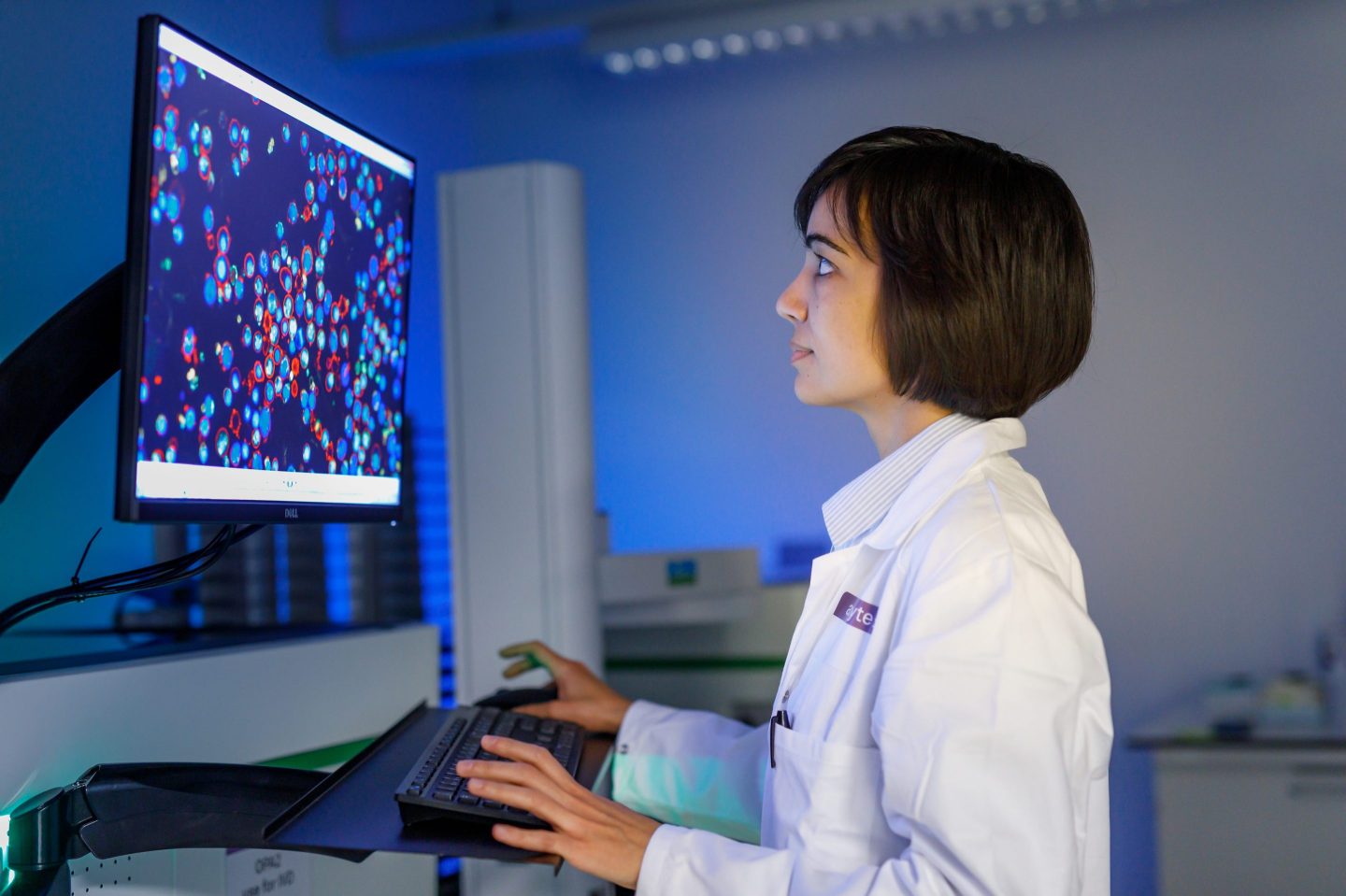 A woman in an Allcyte lab coat looking at images of cancer cells on a screen.