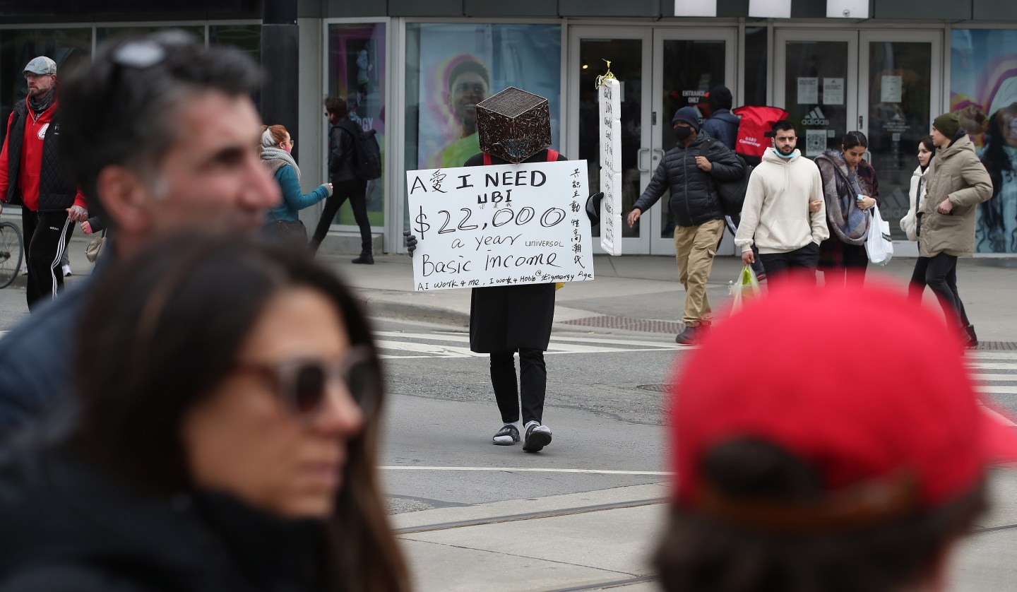 Toronto, ON - March 27 - A masked man walks through the scramble intersection at Yonge and Dundas advocating for universal basic income.
