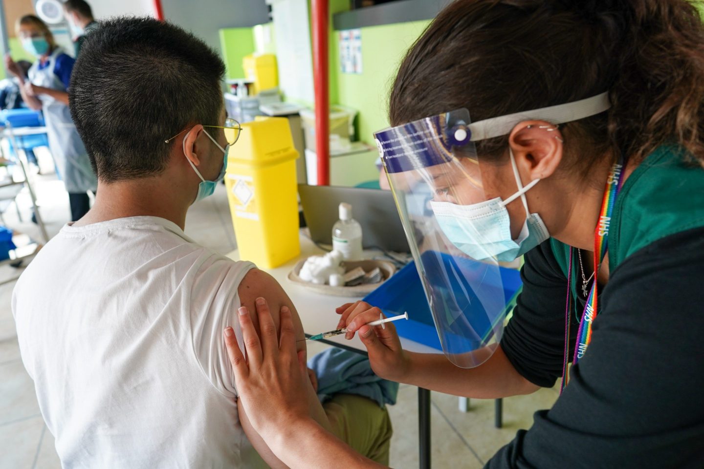 A woman wearing PPE injecting someone's arm.
