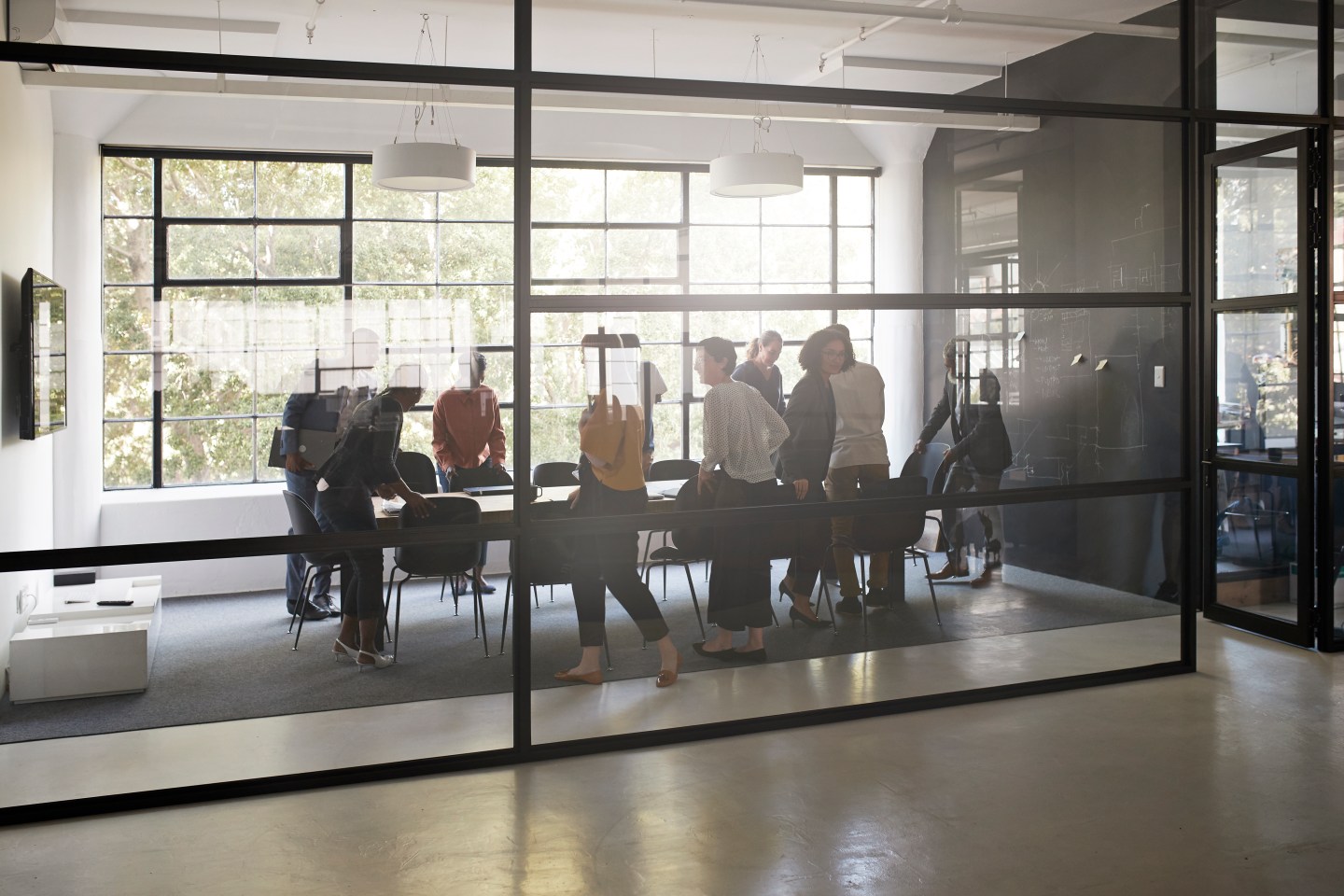 Businessman and businesswoman getting settled in new conference room for meeting seen through transparent wall at workplace