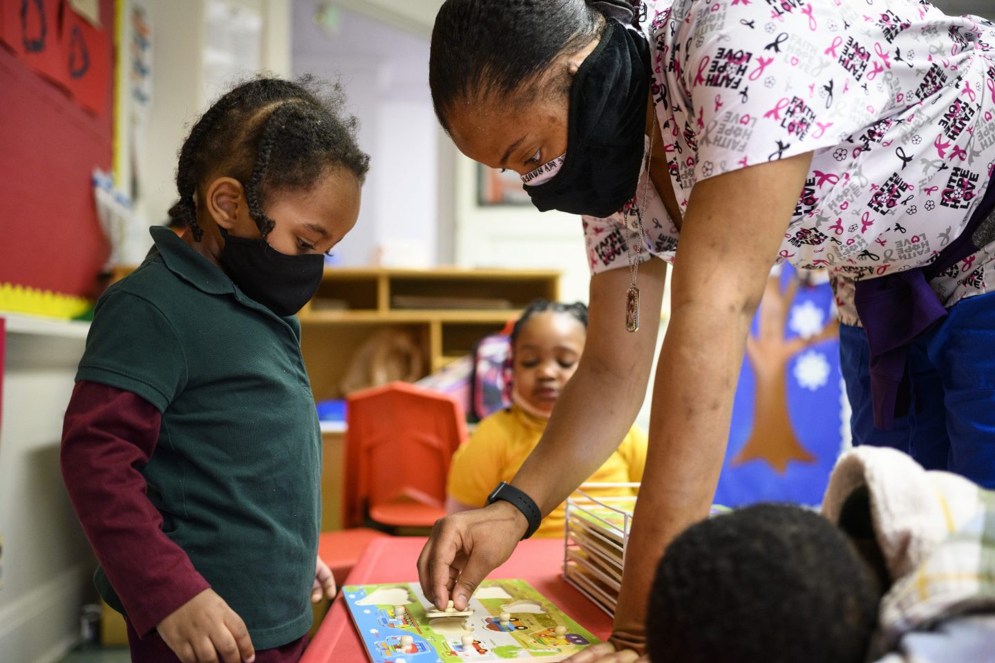 A child care teachers works with a child in the classroom