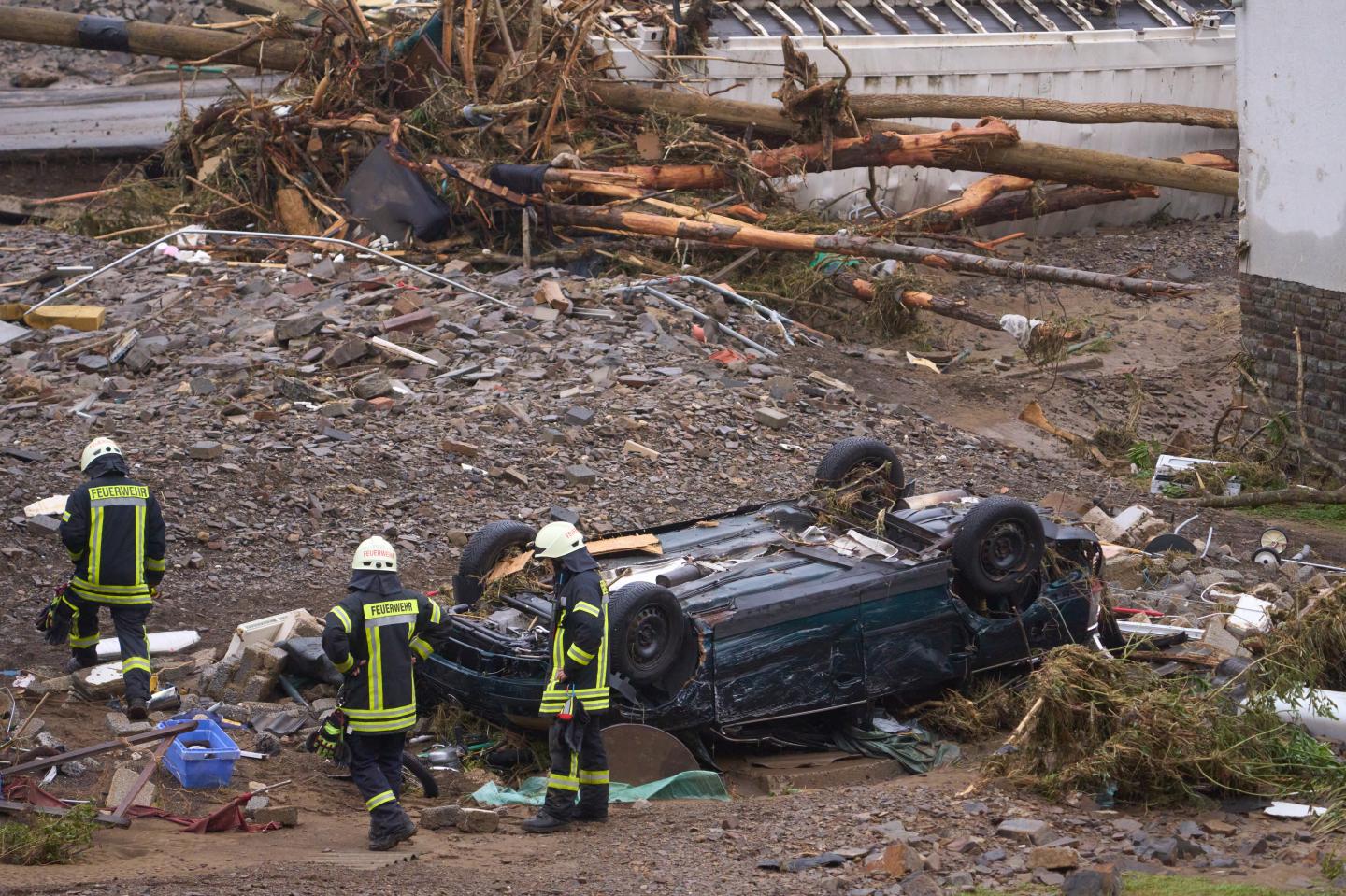 16 July 2021, Rhineland-Palatinate, Bad Neuenahr-Ahrweiler: Firefighters walk past a destroyed car in the community of Schuld the day after the flood disaster.