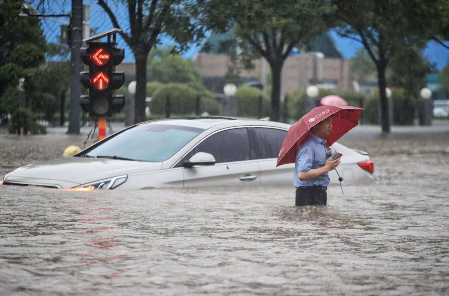 This photo taken on July 20, 2021 shows a man wading past a submerged car along a flooded street following heavy rains in Zhengzhou in China's central Henan province.