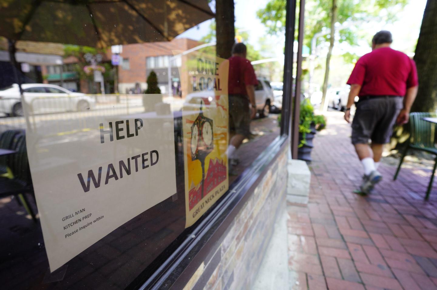 A man walking next to restaurant with a help wanted sign in the window.