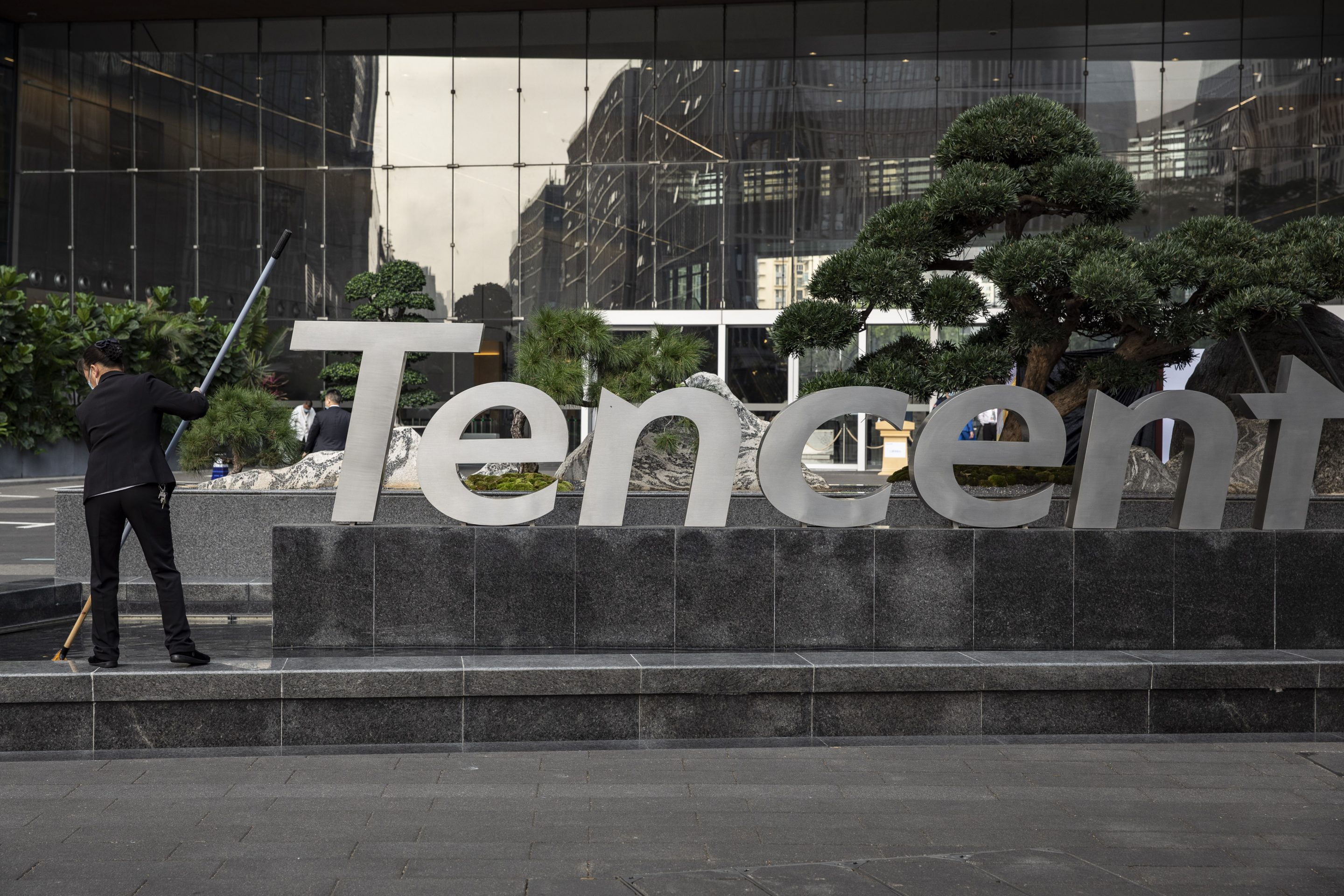 A worker cleans a water feature next to a Tencent Holding Ltd. logo at the company's headquarters in Shenzhen, China, on Saturday, March 20, 2021.