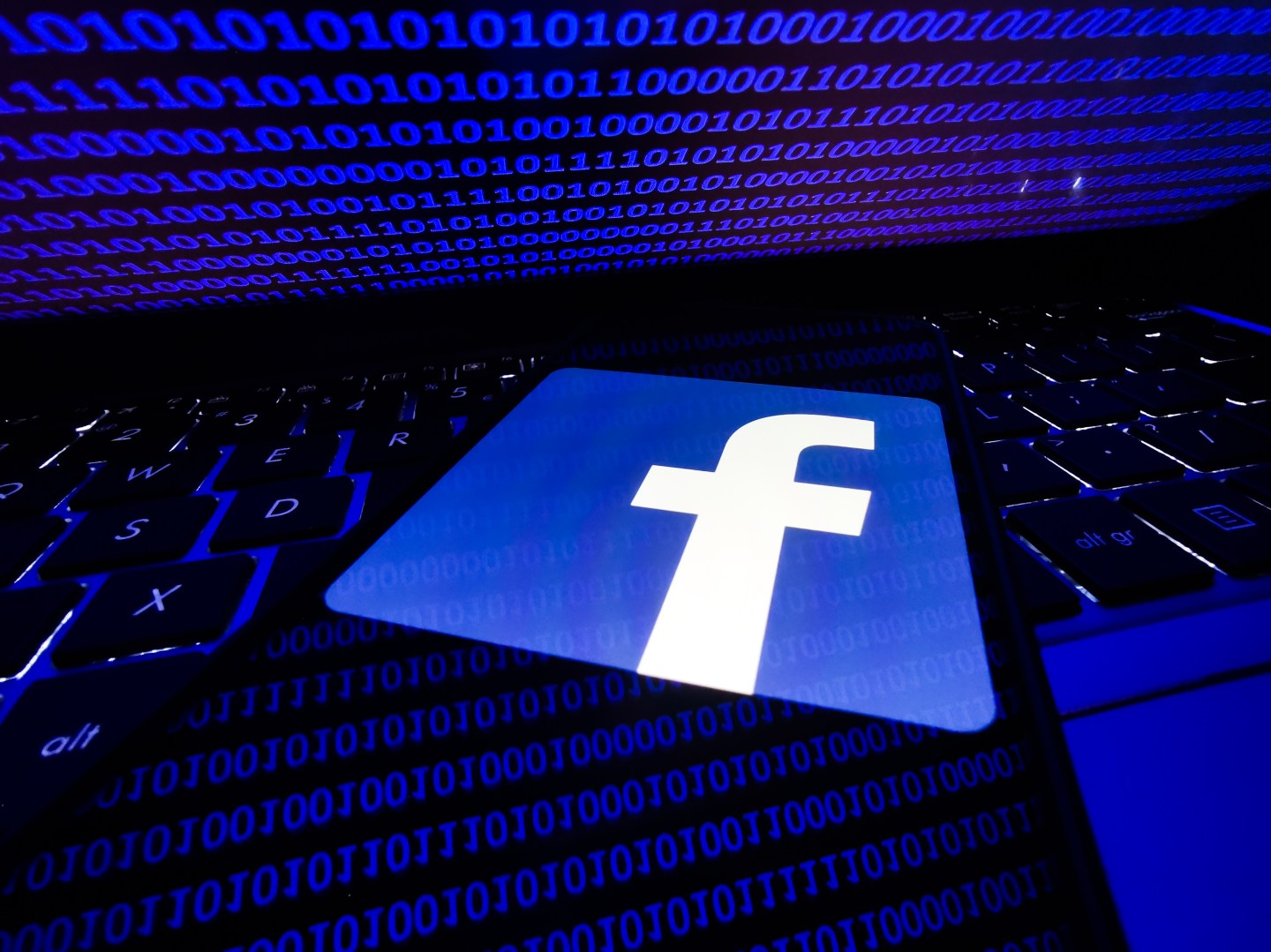 Facebook logo displayed on a phone screen is seen with binary code displayed on a laptop screen in this illustration photo taken in Krakow, Poland on August 17, 2021.