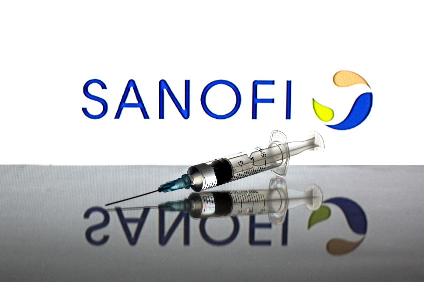 In this photo illustration a medical syringe seen displayed in front of the Sanofi logo.