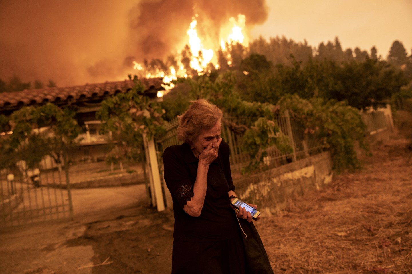 An elderly resident reacts as wildfire approaches her house in the village of Gouves, on the island of Evia, Greece, on Sunday, Aug. 8, 2021.