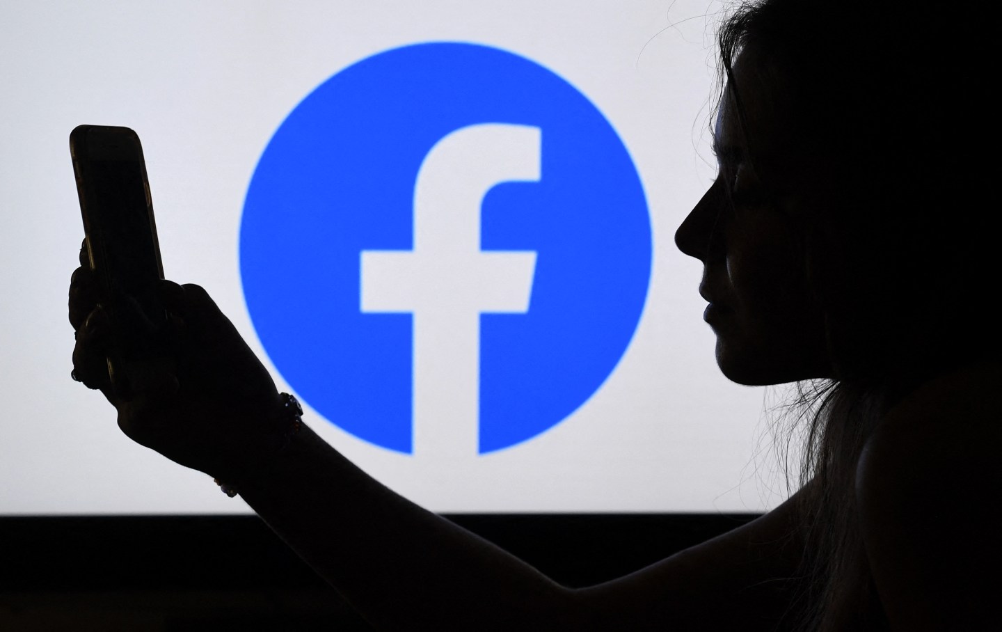 In this photo illustration, a person looks at a smart phone with a Facebook App logo displayed on the background, on August 17, 2021, in Arlington, Virginia.