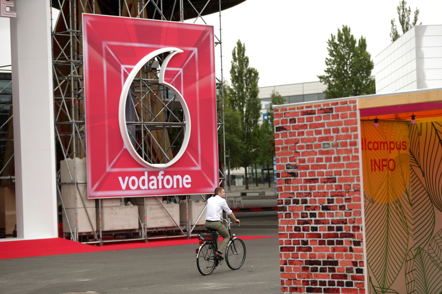 A cyclist rides passed a Vodafone Group Plc logo at the company's exhibition space during the CeBIT 2018 tech fair in Hanover, Germany, on Monday, June 11, 2018.