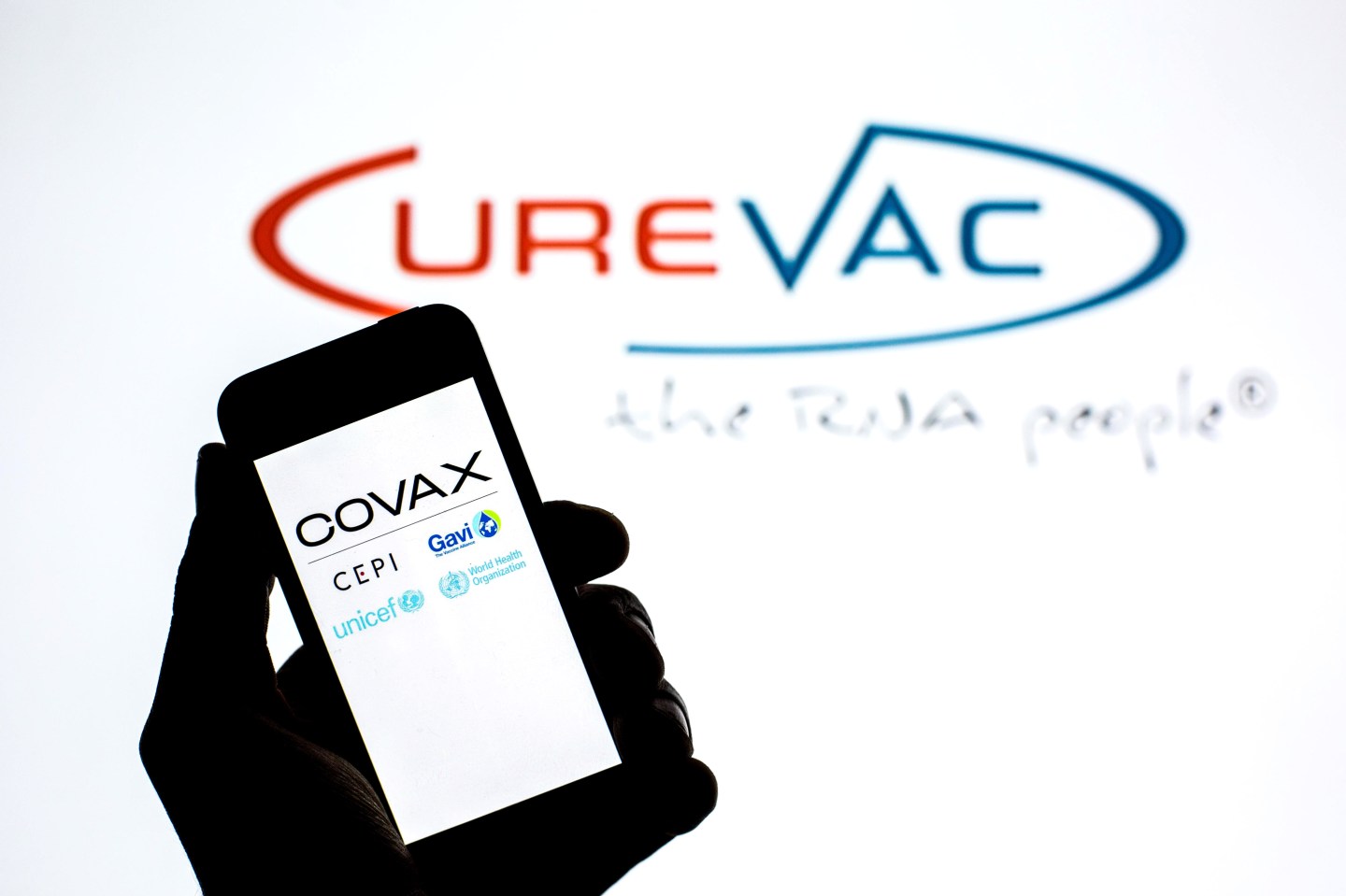 In this photo illustration the Covax Facility logo seen displayed on a smartphone screen with the logo of CureVac in the background.
