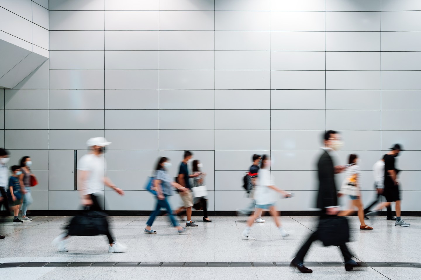 Blurred motion of a crowd of busy commuters with protective face mask walking through platforms at subway station during office peak hours in the city