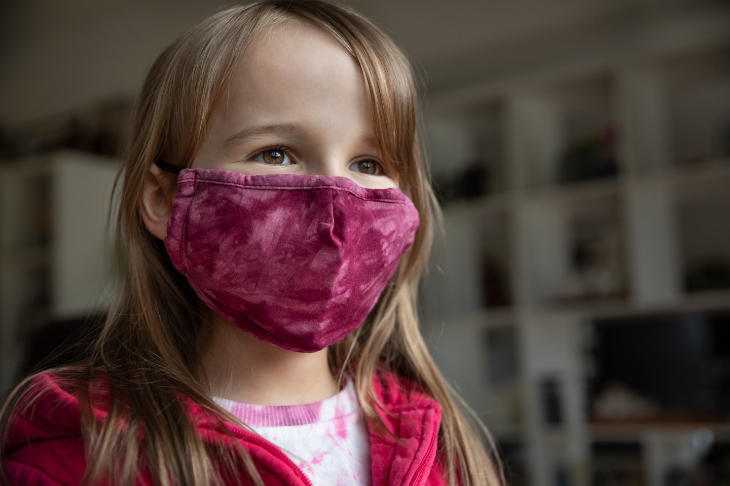 Girl (8-9) smiling behind a pink protective face mask
