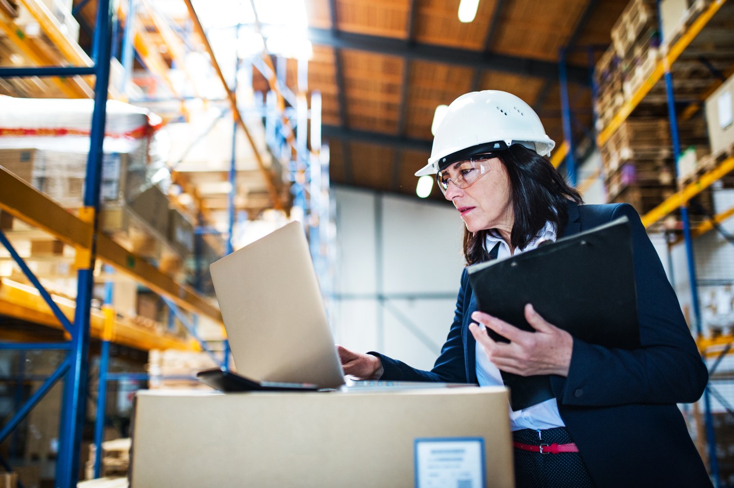 Senior warehouse woman manager or supervisor with a laptop and clipboard, working. Stock controlling.