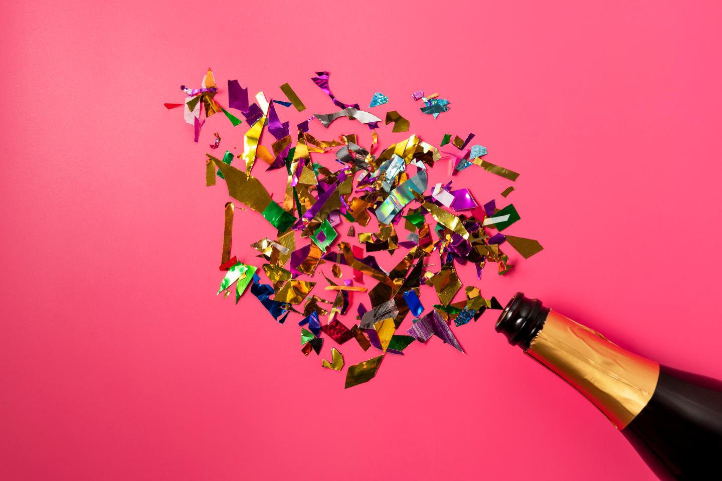 Champagne bottle with confetti on pink background.