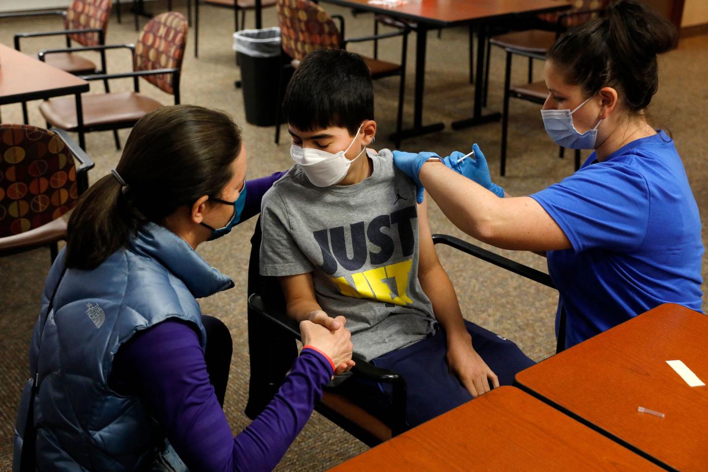 Jamie Blank (L) holds her son, Ari Blank's hand as he receives the Pfizer vaccine.