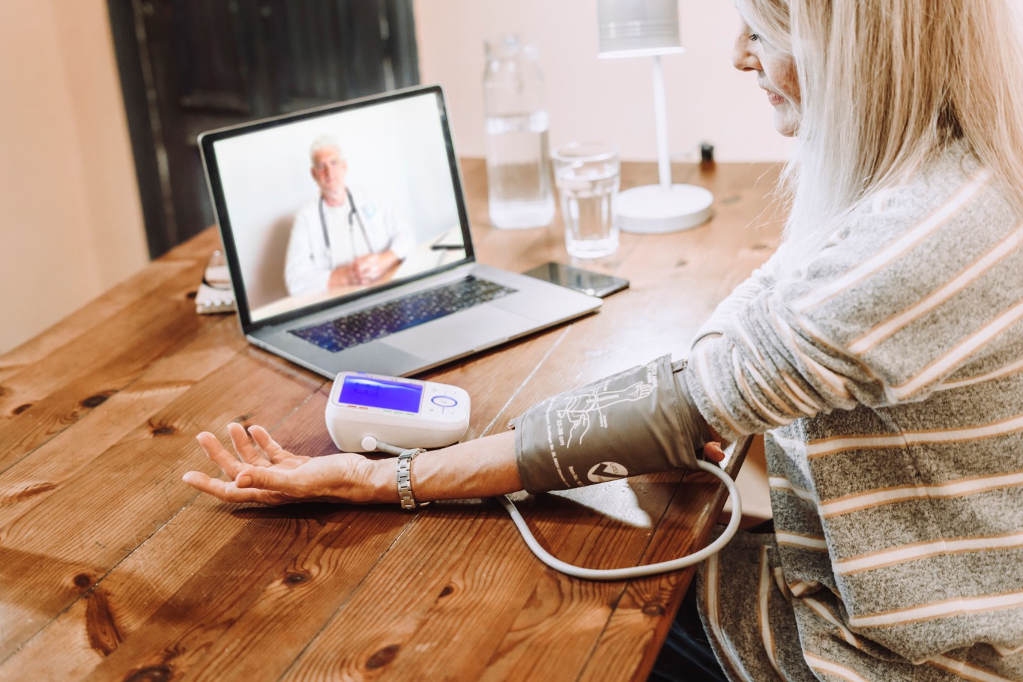 Senior woman checking own blood pressure under guidance of doctor on video call at home