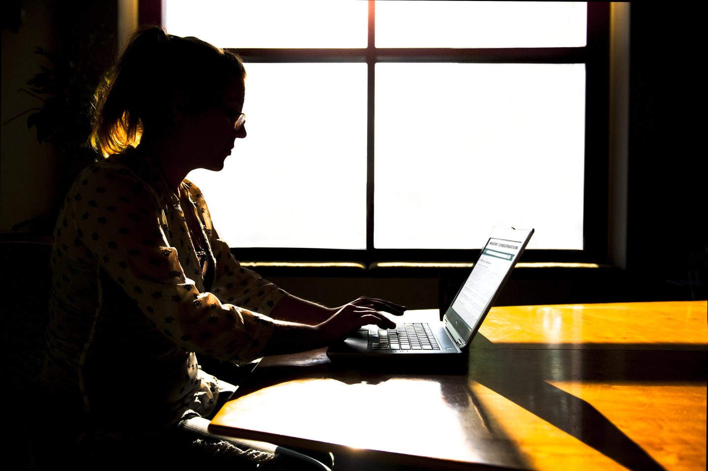 Woman silhouetted at office window.