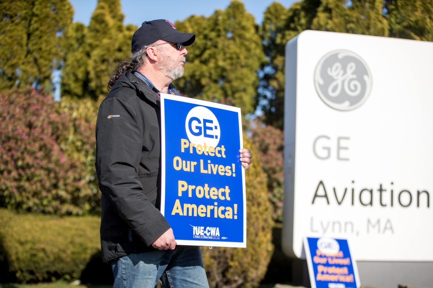 A worker holds a sign during a demonstration outside the GE Aviation facility in Lynn, Mass., after the company announced job cuts in 2020. Some 1,200 workers now remain employed by GE in the facility where skilled machinists and techs build components and engines for the U.S. military.