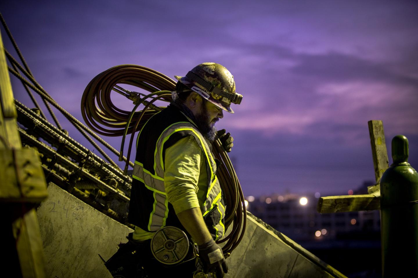 A construction worker carries welding equipment.