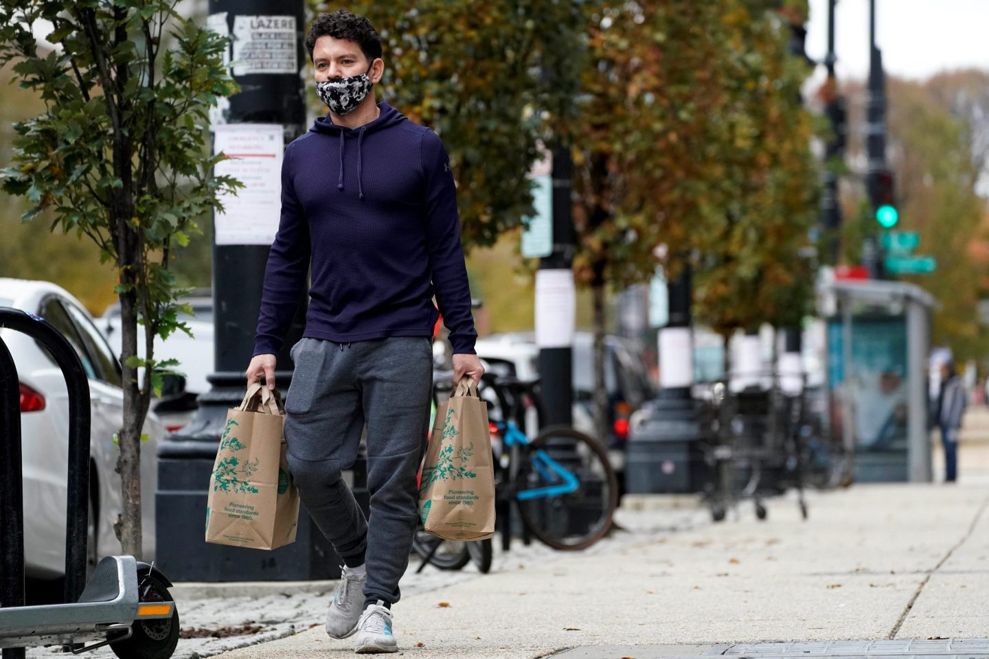 A man walking in the street holding groceries.