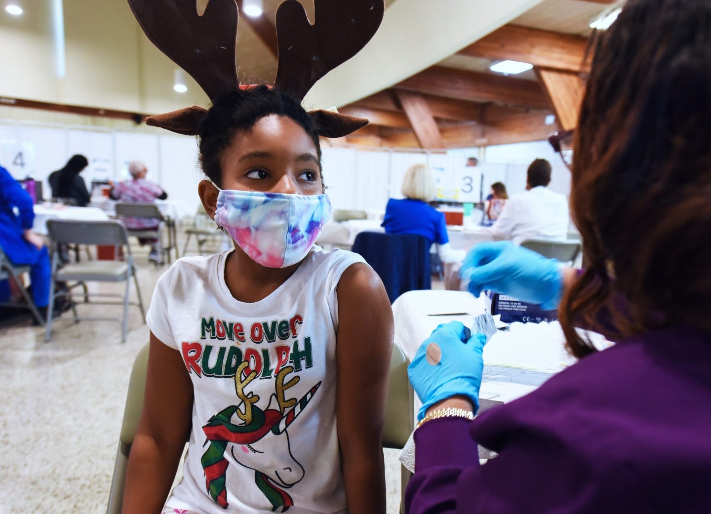 A girl prepares to receive a COVID-19 vaccine dose at the Sanford Civic Center in Sanford, Fla. Thanks to vaccines, the authors write, “COVID-19 will have a much harder time spreading, and effective new treatments will lead to dramatic reductions in deaths in 2022.”