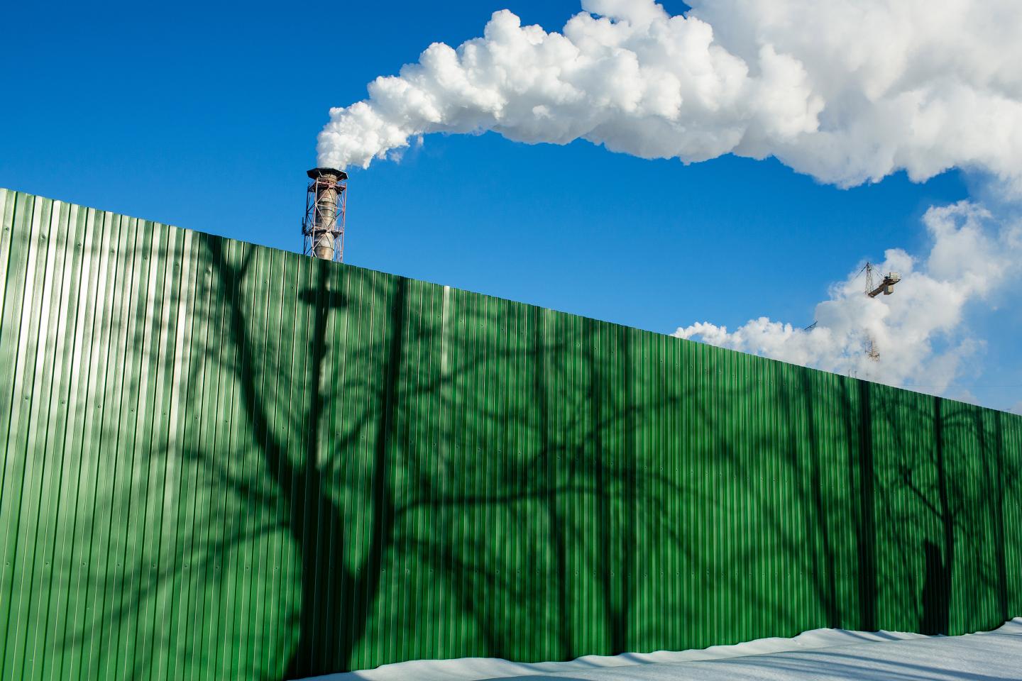 Chimneys emit vapor behind a fence.