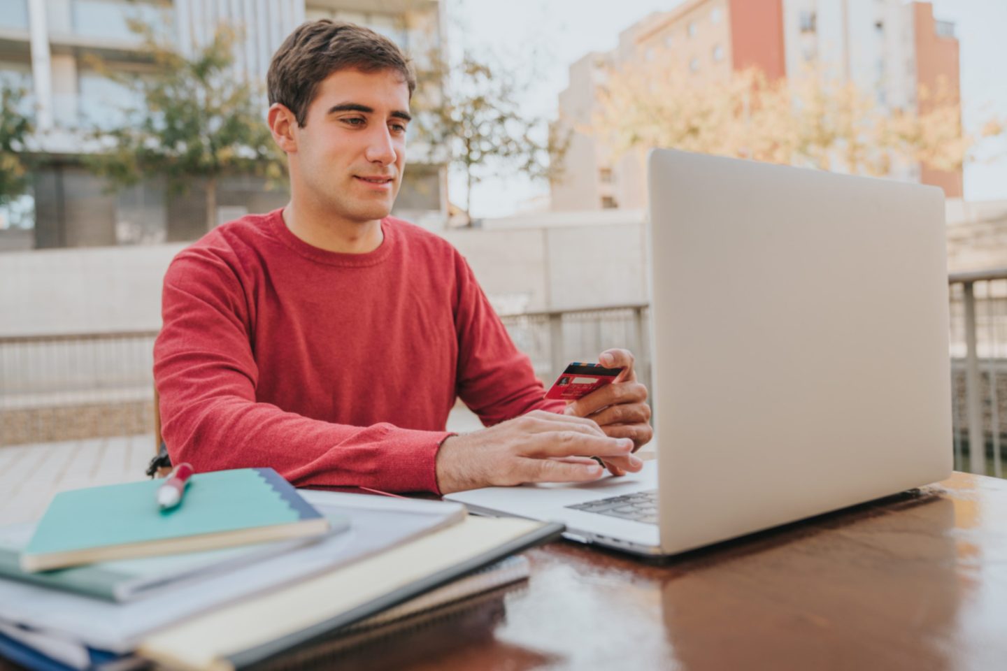 Male student holds a credit card while paying on a laptop