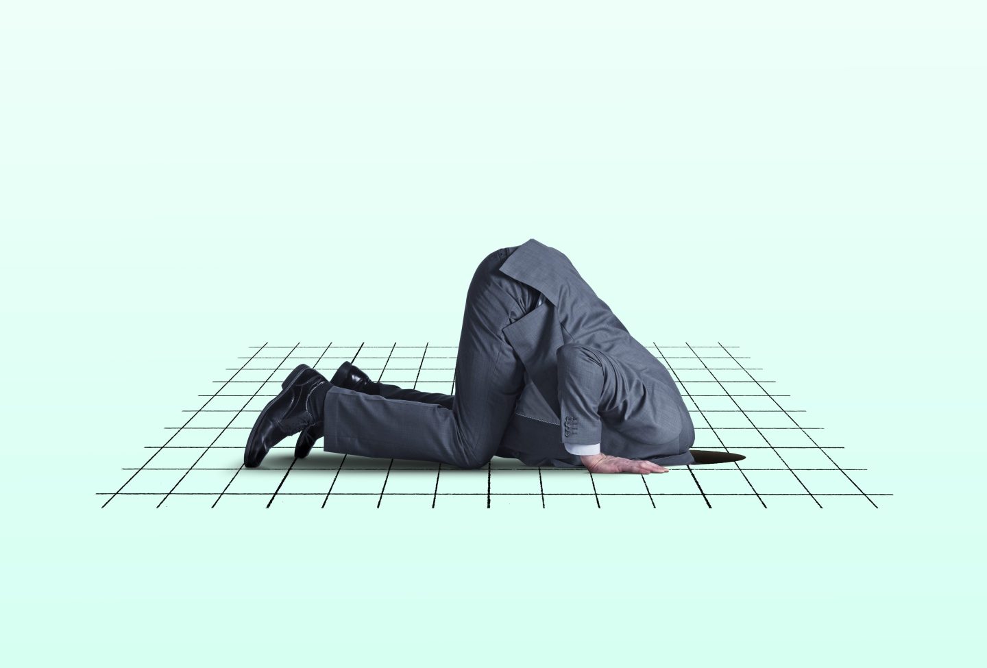 A man kneels on all fours as he places his head into a hole in the ground .
