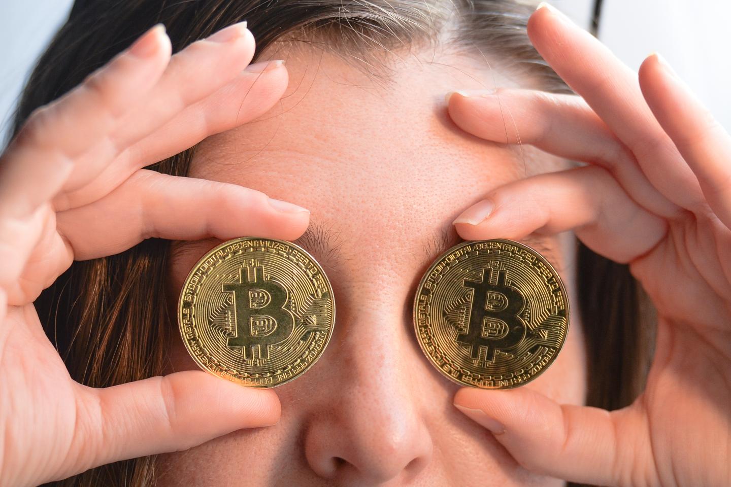 Stock photo of person holding fake Bitcoin coins over eyes.