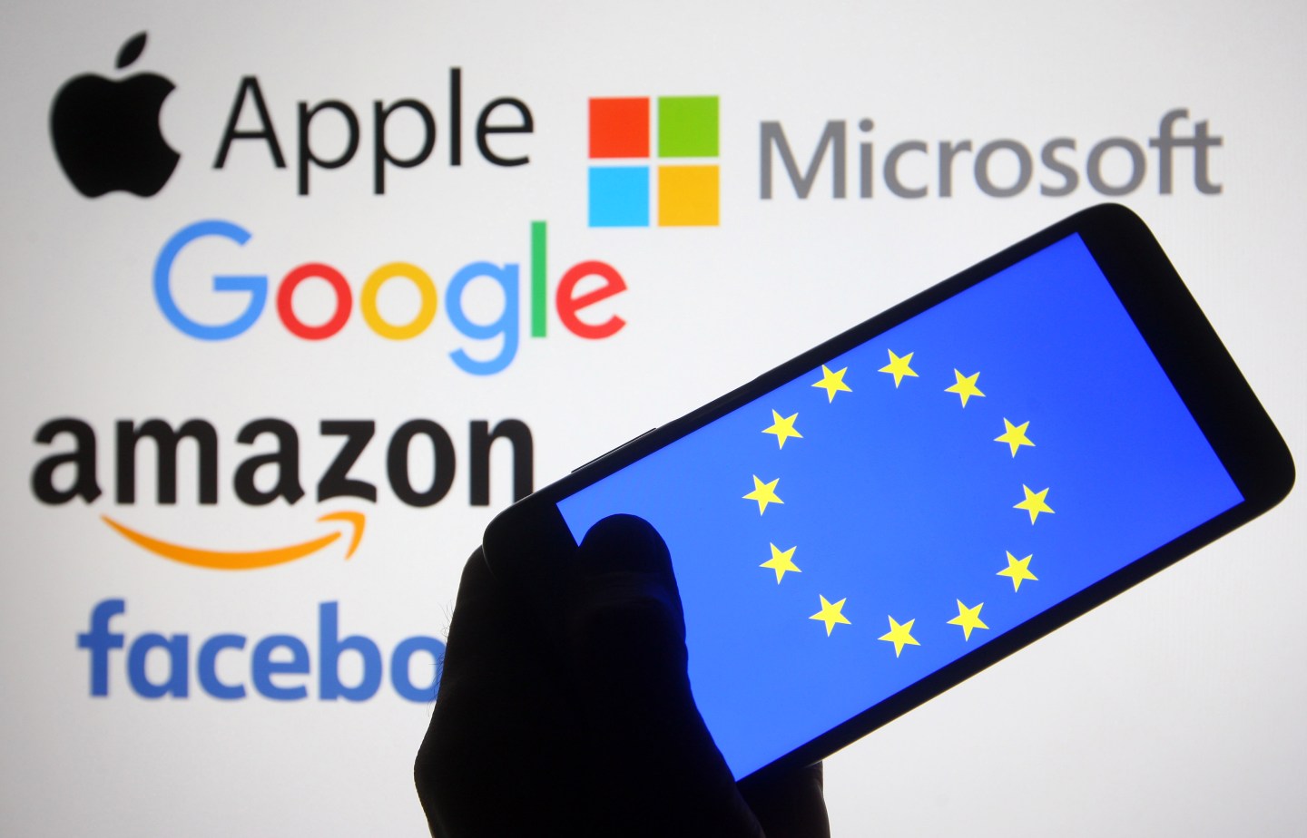 In this photo illustration, the EU (European Union) flag is seen on a smartphone screen in front of Apple, Microsoft, Google, Amazon and Facebook logos.