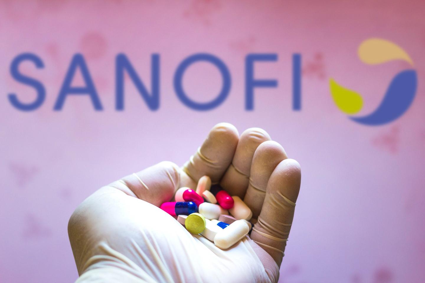 Gloved hand holding pills in front of Sanofi corporate logo