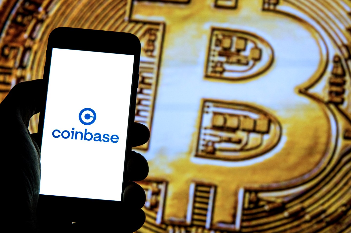 In this photo illustration a Coinbase logo seen displayed on a smartphone with a Bitcoin in the background.