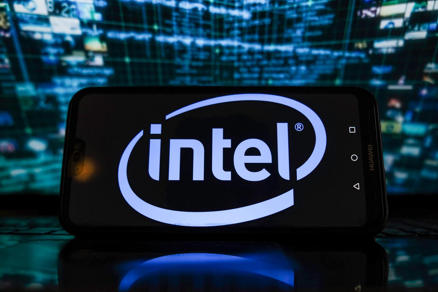 In this photo illustration, an Intel logo is displayed on a smartphone with stock market graphics in the background.