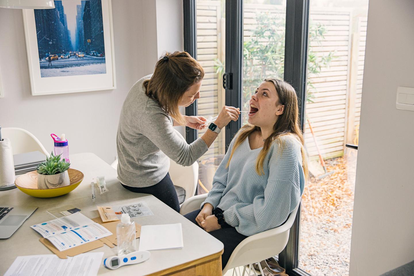 Woman using home COVID-19 testing kit on her teenage daughter.