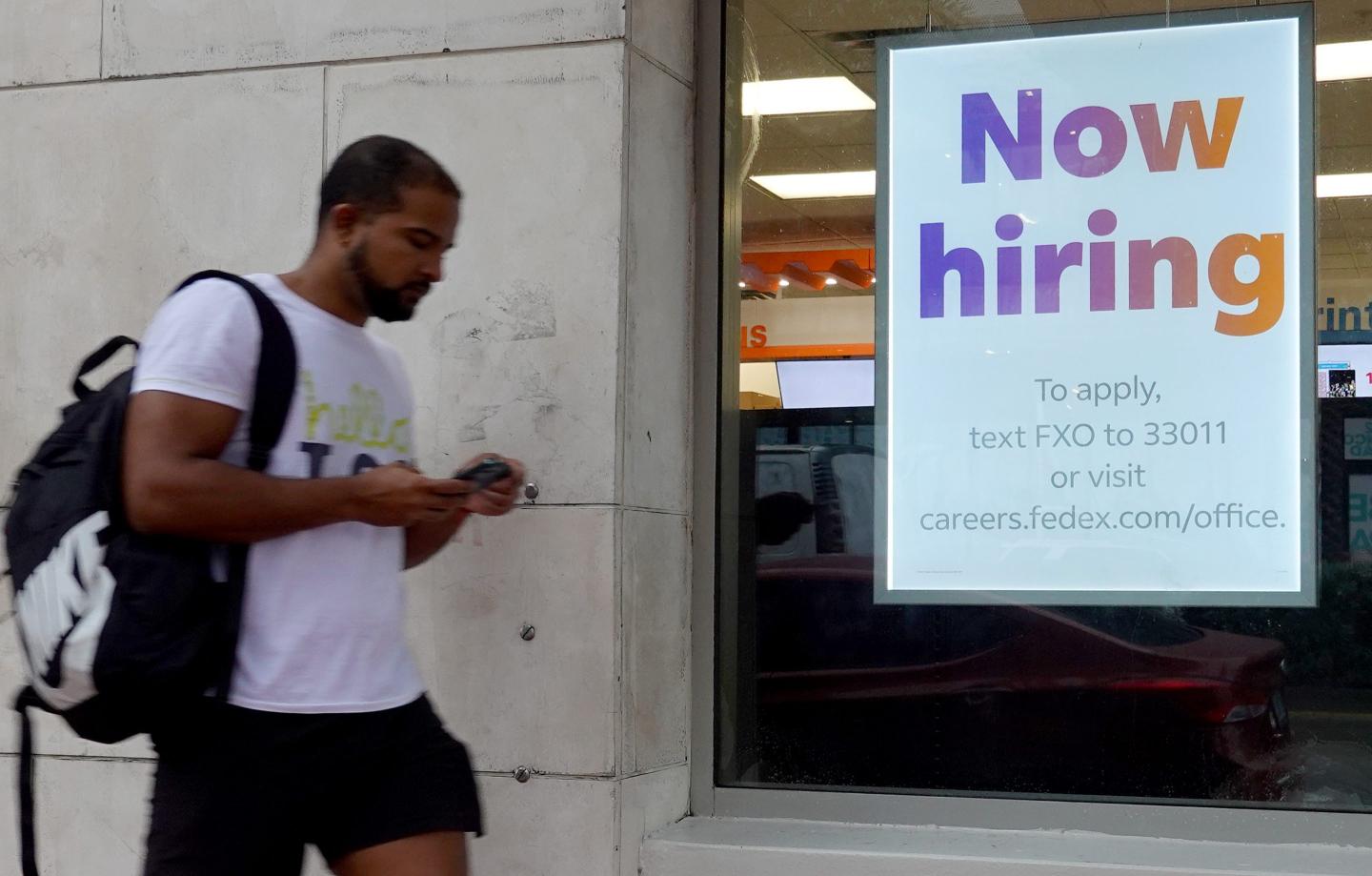 A man walks past a sign that says “Now Hiring.”