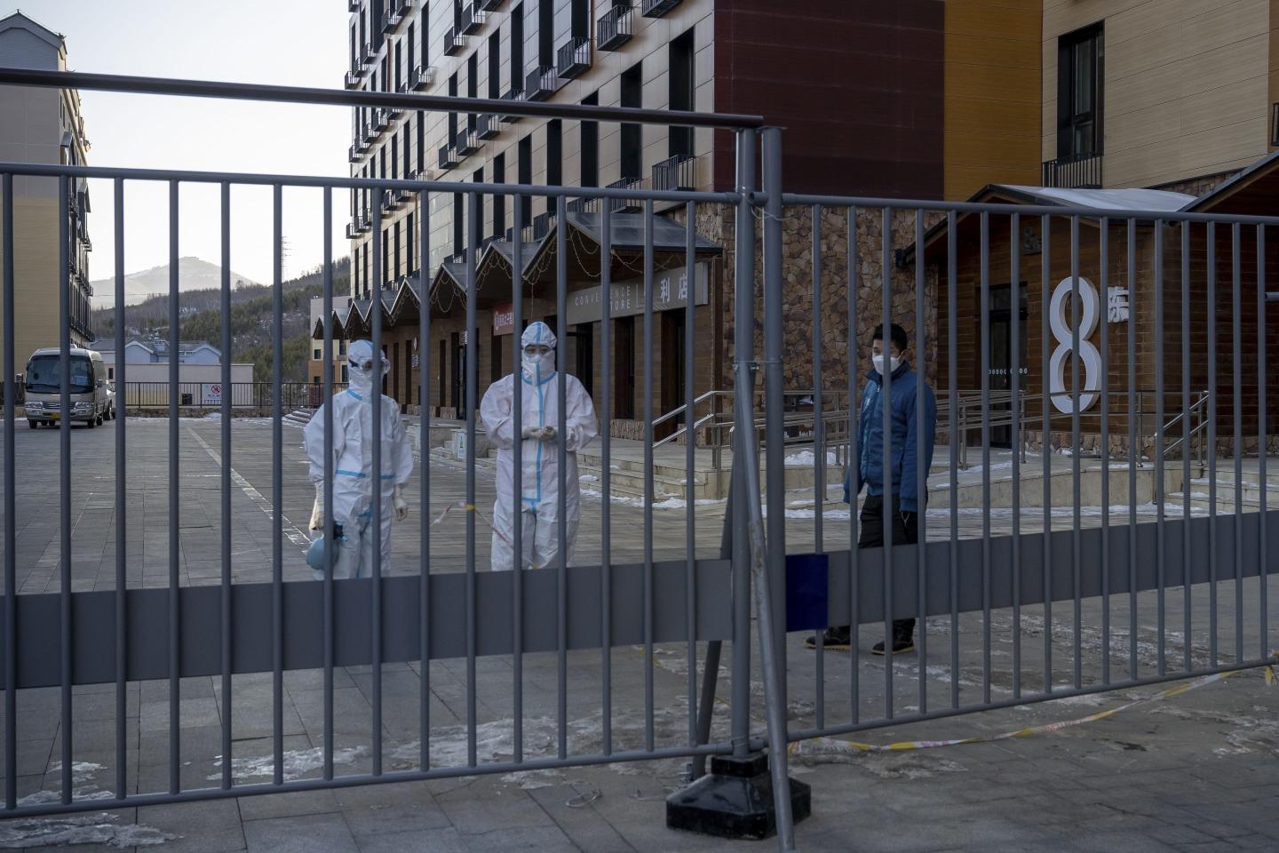 Chinese medical workers wearing PPE stand behind a closed gate.