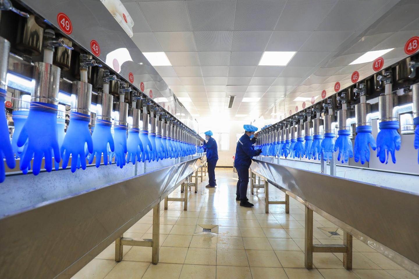 Photo of gloves being inspected by human workers at a rubber glove manufacturing plant in China.