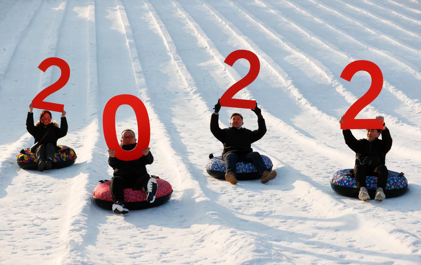 Tourists holding a '2022' sign slide down a slope at Beijing Yuyuantan Park on New Year's Day on January 1, 2022 in Beijing, China.