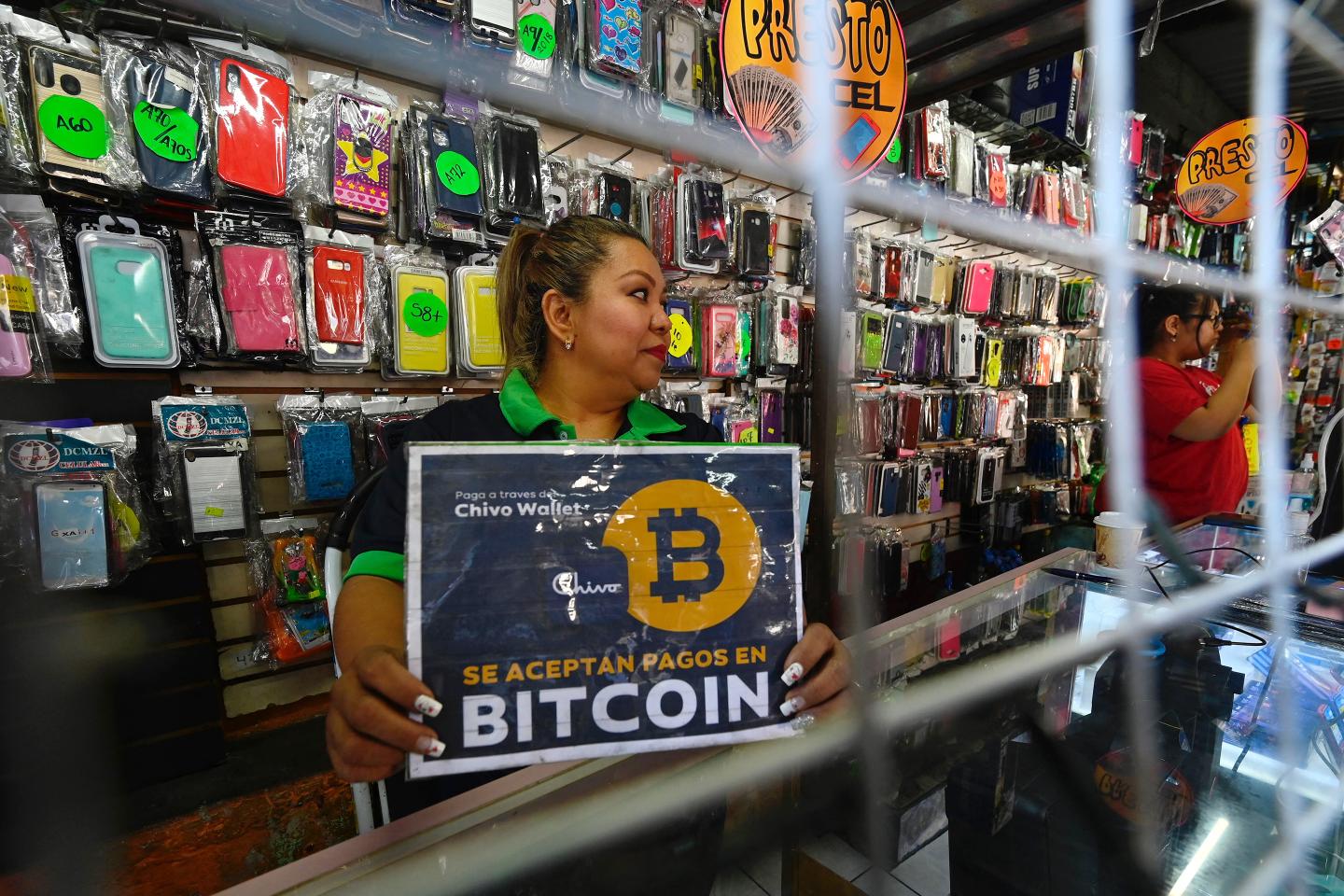 A vendor holds a sign reading "Bitcoin accepted" at a store in San Salvador