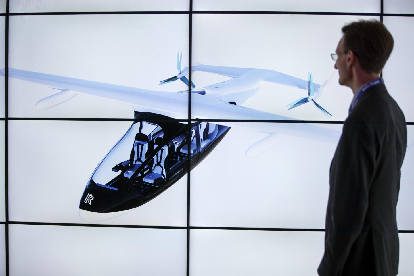 A man poses alongside screens presenting the Rolls-Royce EVTOL air taxi concept during the Farnborough Airshow, south west of London, on July 16, 2018.