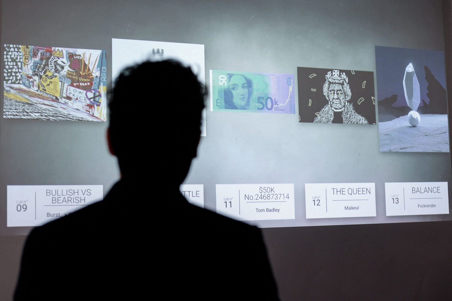 The silhouette of a person looking at NFT artworks.