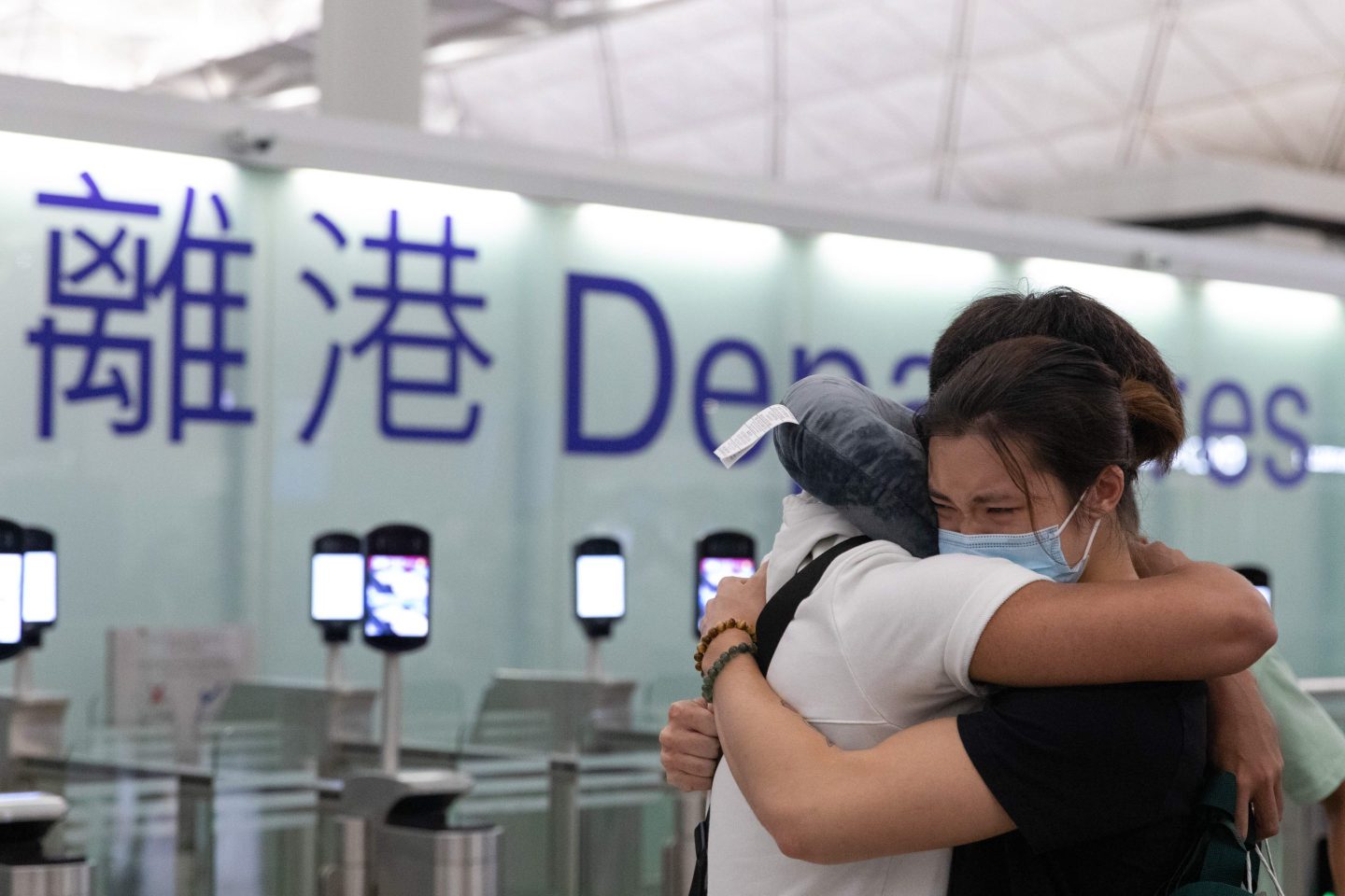 Two people hug in the departures area of Hong Kong airport.