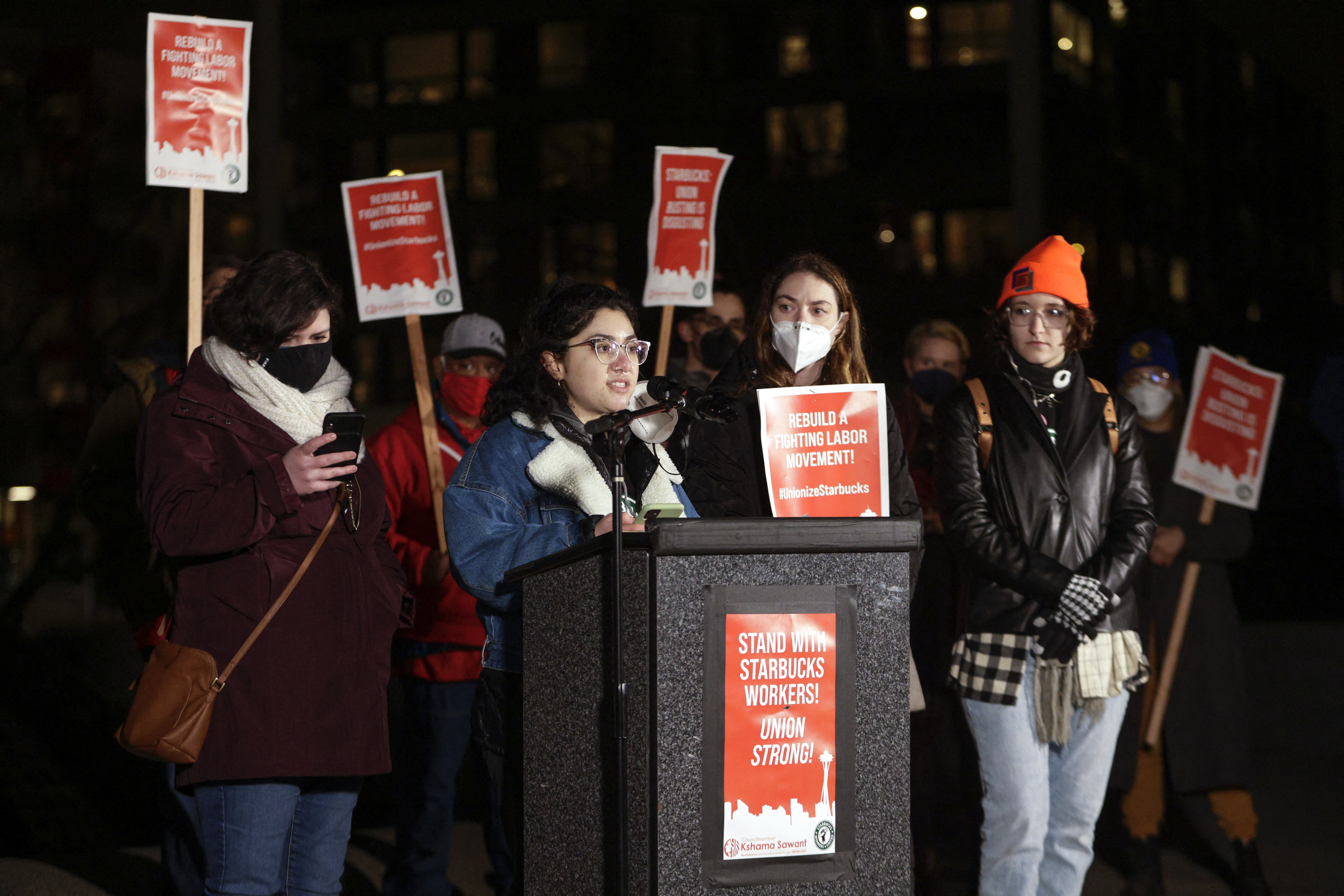 Kyandra Espindola, a barista at one of Seattle's Starbucks locations planning to unionize, speaks as employees Casey Moore and Gianna Reeve of Buffalo, New York, show their support at an evening rally at Cal Anderson Park in Seattle, Jan. 25, 2022. 